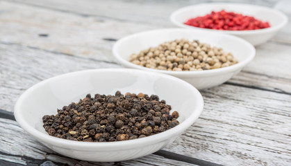 Black, white and pink peppercorn in white bowl over wooden background