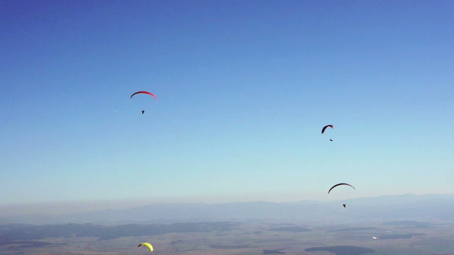 Few paragliders in the blue sky above the green valley