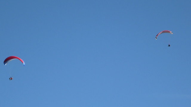 Two paragliders in the blue sky above the mountains