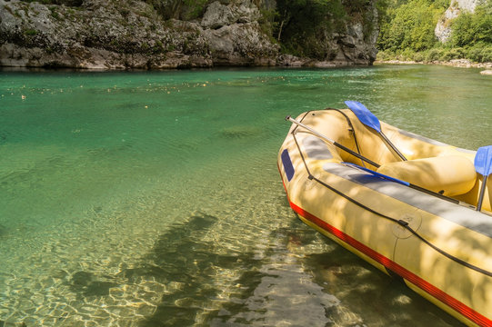 One seven-seater yellow raft with blue paddles on a riverbank in a canyon.