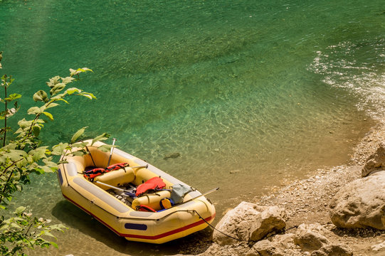 One Seven-seater Yellow Raft With Red Safety Vests And Paddles On A Riverbank In A Canyon.