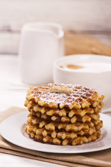 Stack of thick belgium waffles with sugar powder and cup of cappuccino coffee. Tasty breakfast concept. Selective focus