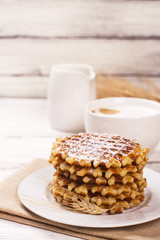 Stack of thick belgium waffles with sugar powder and cup of cappuccino coffee. Tasty breakfast concept. Selective focus