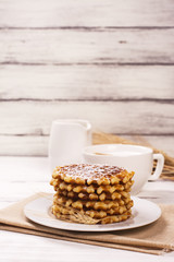 Stack of thick belgium waffles with sugar powder and cup of cappuccino coffee. Tasty breakfast concept. Selective focus