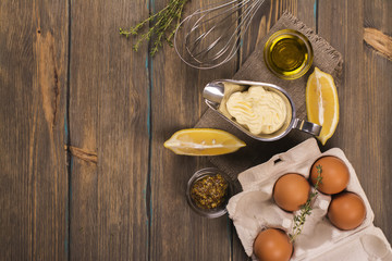 Homemade mayonnaise sauce with ingredients on brown wooden table. Top view