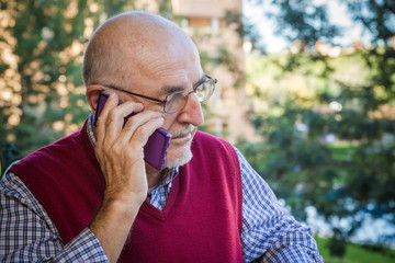 SENIOR MAN USING CELL PHONE ON A PARK BACKGROUND, IN SPAIN