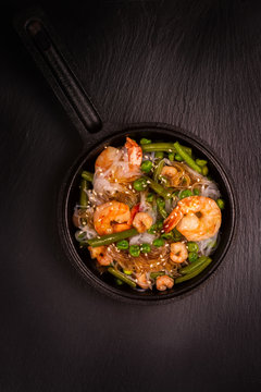 Glass noodle with shrimps and green vegetables in cast-iron pan. Healthy food concept. Top view. Toned image