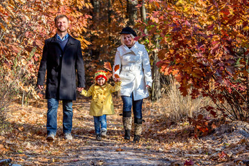 Two Generation Family Walking in Colorful Autumnal Forest Alley Smiling Father Mother Holding Hands of Little Baby Girl Bright Casual Clothing Front View