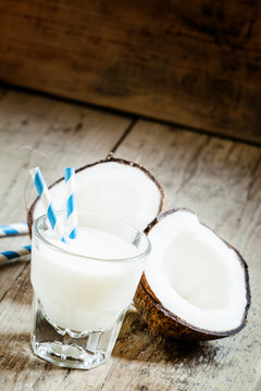 Coconut milk in a glass with striped straw and coconut halves, s
