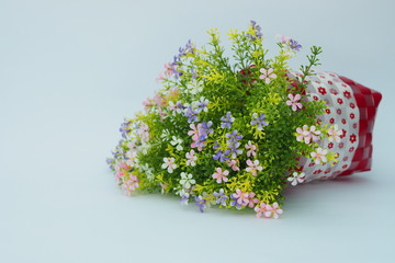 Small colorful artificial flowers with green leafs in a red and white webbed basket