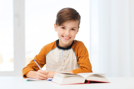 smiling student boy writing to notebook at home