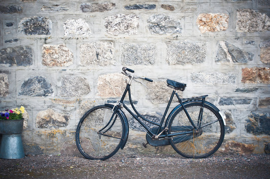 Old rusting bicycle leaning against a stone wall