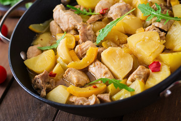 Stewed potatoes with meat and vegetables in a roasting tin on a wooden background