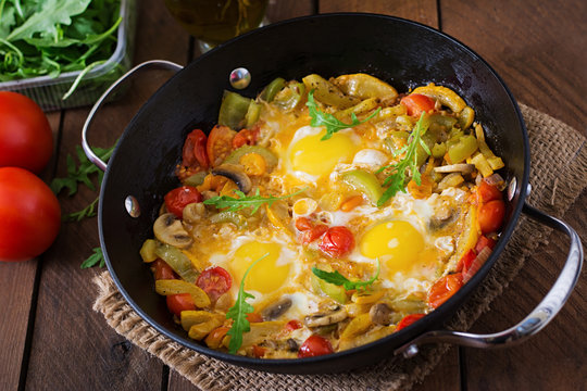 Fried eggs with vegetables in a frying pan on a wooden background