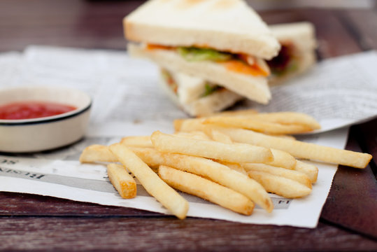 Sandwich with French fries, ketchup and glass of beer.
