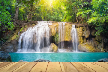 Waterfall, green forest in Erawan National Park in Thailand montage with wooden floor. Landscape with water flow, tree, river, stream and rock at outdoor. Beautiful scenery of nature for vacation.