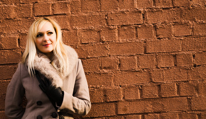 portrait of blonde girl in warm coat over a brick wall