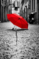 Red umbrella on cobblestone street in the old town. Wind and rain - obrazy, fototapety, plakaty
