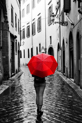 Woman with red umbrella on retro street in the old town. Wind and rain