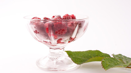 Frozen raspberries in a glass and a green leaf isolated on white background