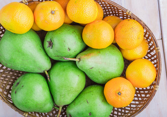 Fresh pears and tangerines in wicker basket on white table