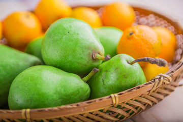 Fresh pears and tangerines in wicker basket on white table