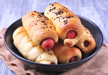 sausage baked in pastry in a black plate on a light wooden background