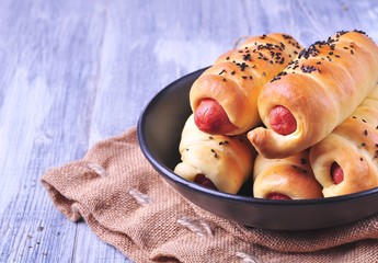 sausage baked in pastry in a black plate on a light wooden background