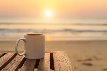 Foto op Canvas Koffiekopje op houten tafel bij zonsondergang of zonsopgang strand © SKT Studio