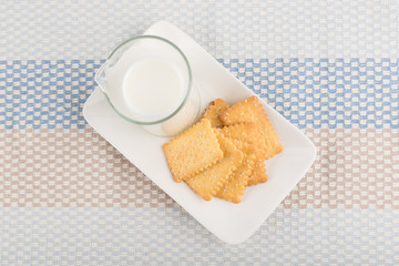 Fresh milk in glass jug and biscuits placed in a white dish, on a striped tablecloth