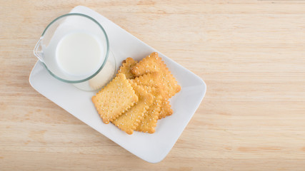 Fresh milk in glass jug and biscuits placed in a white dish, on wooden background