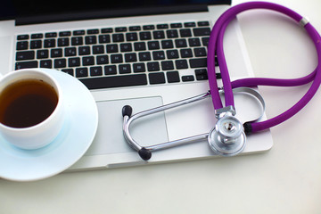 A medical stethoscope near a laptop on a wooden table, on white