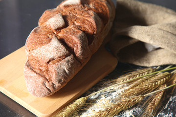 rustic crusty bread and wheat ears on a dark wooden table
