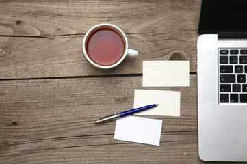 Blank business cards with pen, laptop and tea cup on wooden office table