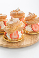 fresh cream puff with whipped cream mint and strawberries on white plate and white wood table