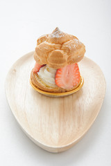 fresh cream puff with whipped cream mint and strawberries on white plate and white wood table