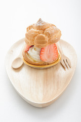 fresh cream puff with whipped cream mint and strawberries on white plate and white wood table