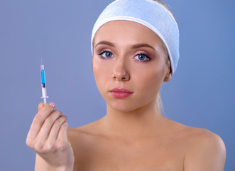 Young beautiful woman with syringe in her hand. Isolated on gray background