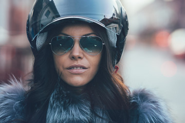 City lifestyle closeup portrait of young woman with motorcycle helmet and sunglasses. Woman seriously watching at camera. Post processed to match old film look.