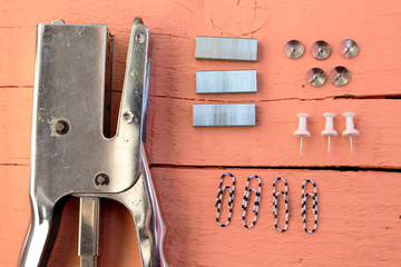 Office material placed on wooden background - stapler, pins, rolled paper, paper clip and staple's wires