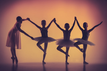 Obraz premium Three little ballerinas dancing with personal ballet teacher in dance studio