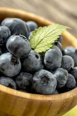 Wooden bowl full of ripe juicy blueberries garnished with a gree