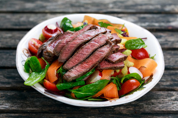 Spicy Beef Slices Meat Salad with Carrots, Tomatoes, Cucumber, Parsley and Salad leaves Spinach, rocket, red ruby chard on old wooden table