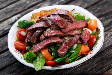 Spicy Beef Slices Meat Salad with Carrots, Tomatoes, Cucumber, Parsley and Salad leaves Spinach, rocket, red ruby chard on old wooden table