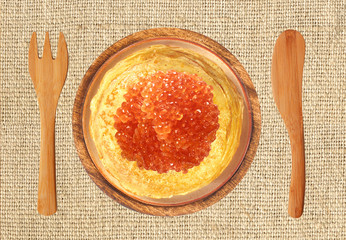 Delicious pancakes with red caviar on wooden plate, fork and kni