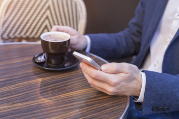 Young adult using mobile phone on restaurant terrace with coffee