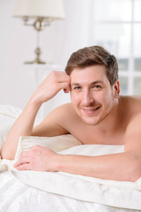 Young man in bed rests against a pillow.