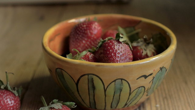 Ripe, fresh strawberries in a ceramic bowl on a rustic wooden table perfect for a healthy breakfast - dolly shot