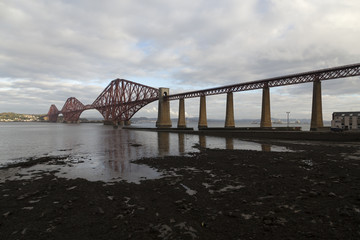 A bridge for trains over some water with a shore line in the foreground