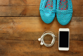top view of woman shoes anmd smartphone whith earsphones over wooden background